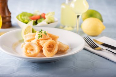 Geleneksel İtalyan kızarmış kalamar ve limon dilimi beyaz tabakta servis edilir.