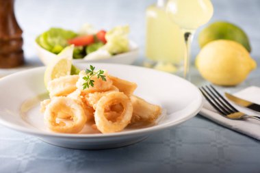 Geleneksel İtalyan kızarmış kalamar ve limon dilimi beyaz tabakta servis edilir.