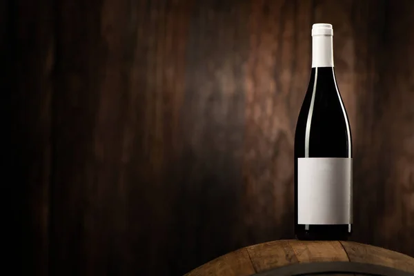 A Red wine bottle on wodden barrel with a wooden backgorund close up