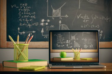 School supplies with digital laptop on wooden table with a blackboard on background