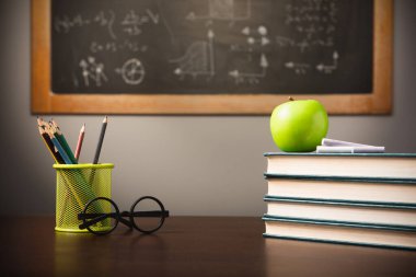 Back to school background with books, pencils and apple over chalkboard and wooden table close up