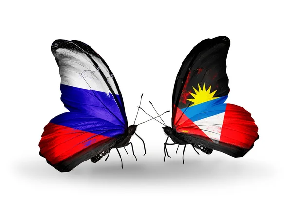 Dva motýli s vlajkami Ruska a antigua a barbuda na křídlech — Stock fotografie