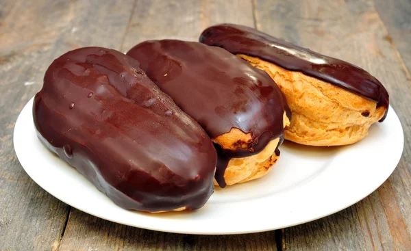 Cakes "eclairs" in the plate on wooden table — Stock Photo, Image