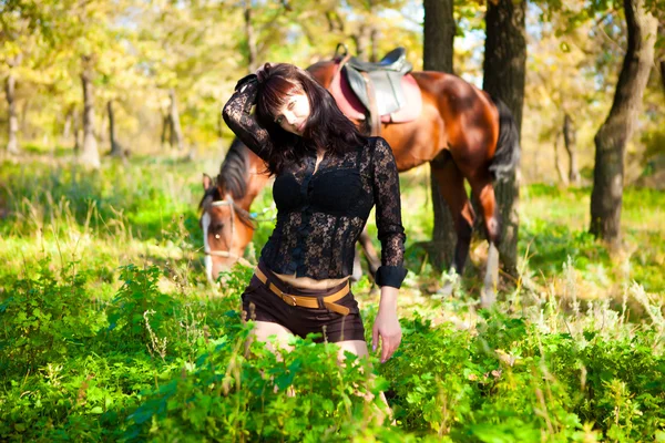 Menina bonita jovem posando enquanto deitado em um fundo de floresta e cavalos — Fotografia de Stock