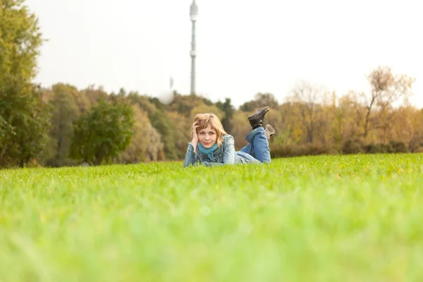 Menina em jeans roupas encontra-se em um gramado de grama verde no parque — Fotografia de Stock