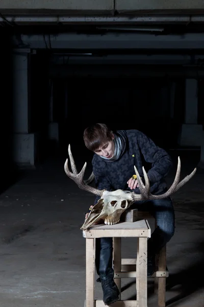 Young man working with a sharp deer skull in a dark basement — Stock Photo, Image