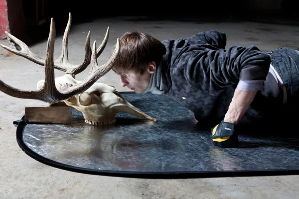 Young man lying down looking at the deer skull in a dark basement — Stock Photo, Image
