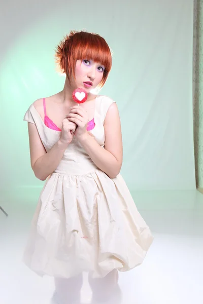 Tjej med rött hår med lollipop i vit klänning på turkos bakgrund — Stockfoto
