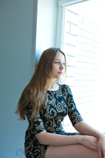 Junges schönes Mädchen in schwarzem Kleid sitzt am Fenster — Stockfoto