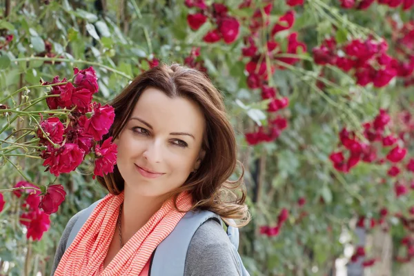 Beautiful woman in garden under red roses bower — Stock Photo, Image