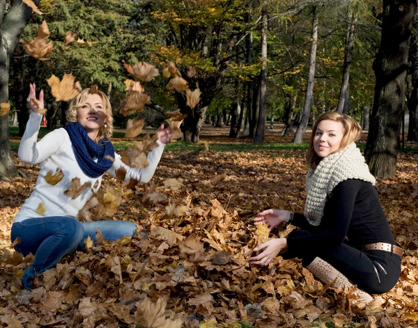 Two beautiful young women throwing yellow leaves — Stock Photo, Image