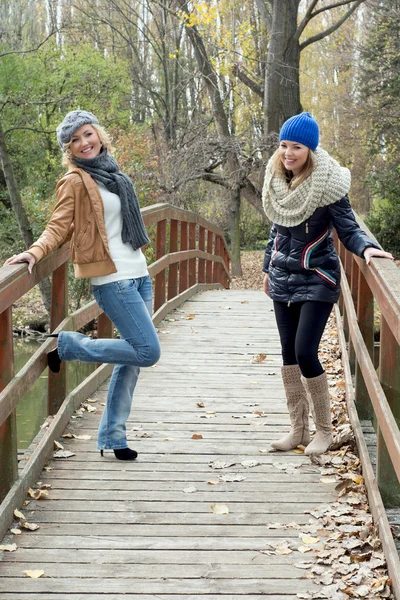 Two attractive young women laughing on a wooden bridge — Stock Photo, Image