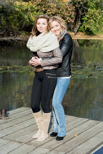 Dwa piękne młode kobiety i staw w parku jesień — Zdjęcie stockowe