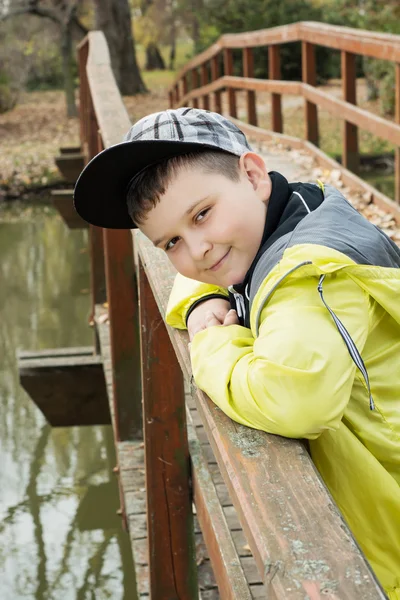 Giovane ragazzo in berretto da baseball in piedi sul ponte e sorridente — Foto Stock