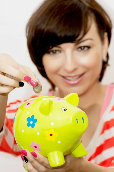 Young woman gives a euro coin into decorative ceramic piggy bank — Stock Photo, Image