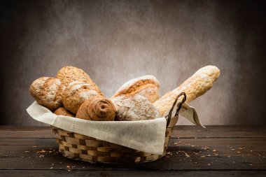 Ahşap masada saman sepetinde pişmiş ekmek çeşitleri.