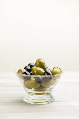 Büyük yeşil ve siyah zeytinler cam kasede, ahşap masada.