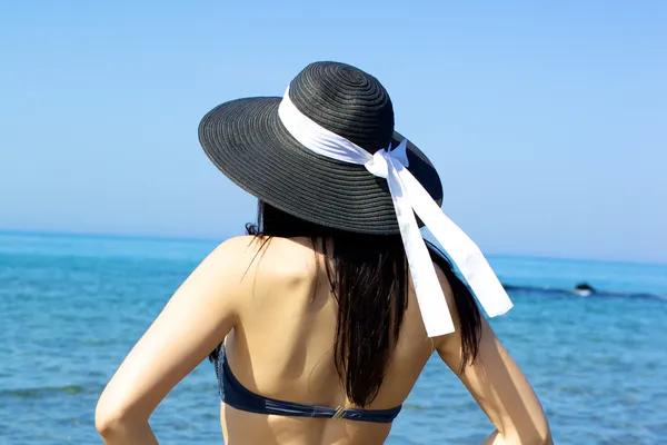 Mujer mirando horizonte con sombrero frente al hermoso mar azul — Foto de Stock