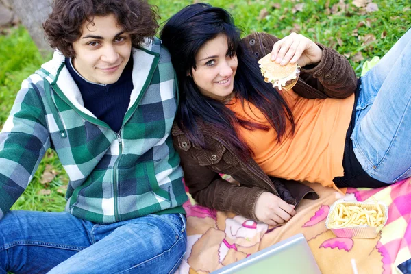 Happy couple eating hamburger in parc in the summer — Stock Photo, Image