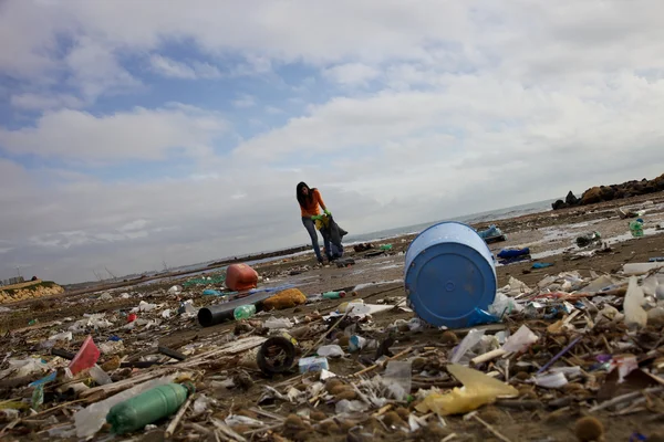 Jonge vrouw met zak probeert te schoon strand vol dump vuil en industriële puinhoop — Stockfoto