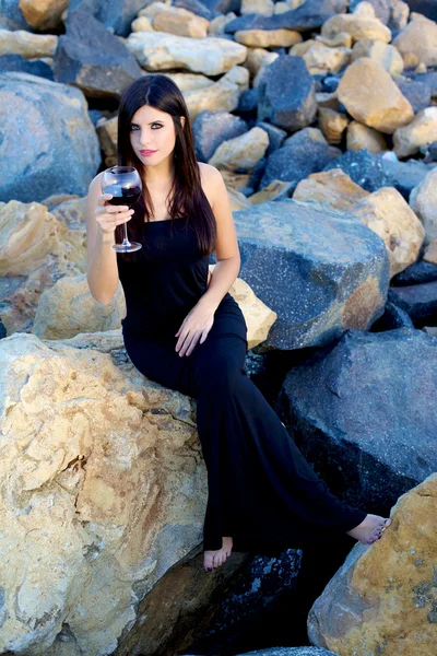 Donna che festeggia con vino rosso seduto sulle rocce — Foto Stock