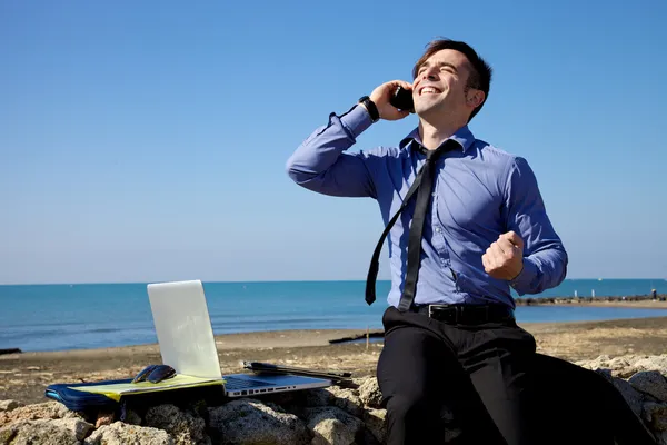Businessman celebrating deal on the phone in front of the ocean — Stock Photo, Image