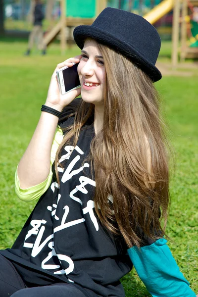 Adolescente chica con sombrero en el parque hablando por teléfono —  Fotos de Stock