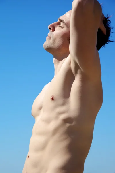 Homem com corpo perfeito com olhos fechados na frente do céu — Fotografia de Stock