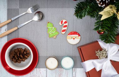 Bir fincan kahve, şeker kaplı bisküviler, kokulu mum ve kırmızı bir hediye kutusu ile Noel yemeği masası süslemeleri..