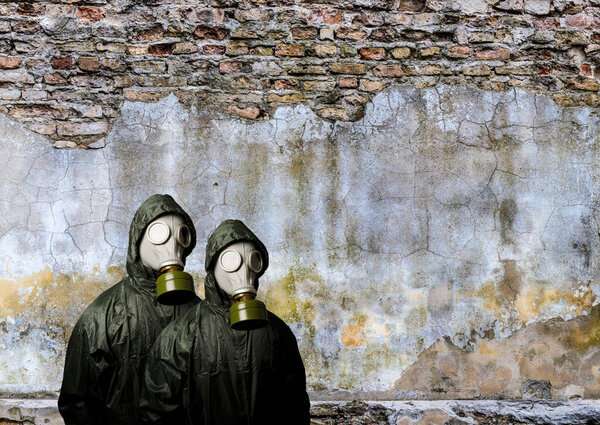 Газовые маски. Два человека в противогазах и кирпичная стена позади с копировальным местом. Опасность химического оружия.