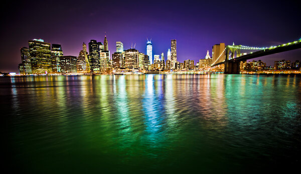 Lower Manhattan and Brooklyn Bridge in New York City at night with reflection in water
