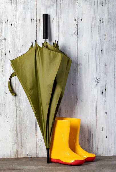 Grönt Paraply Och Gummistövlar Mot Trävägg — Stockfoto