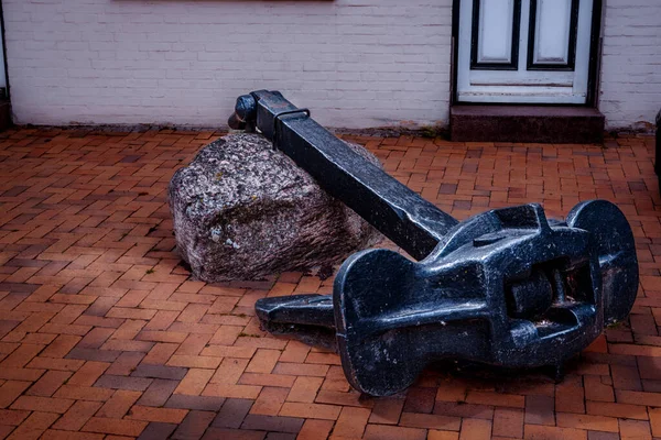 Close up of a big black anchor laying on the ground near a white big stone in the backyard. Germany.