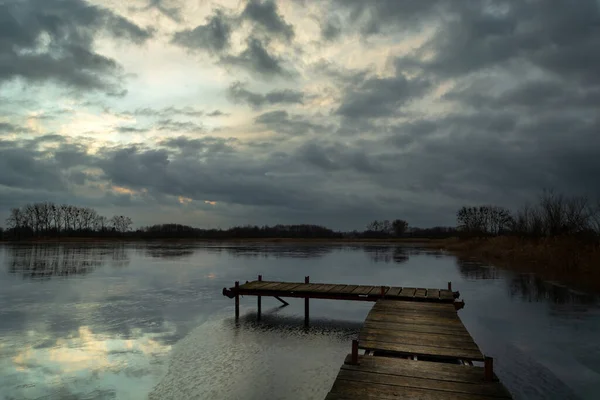 Een pier op een bevroren meer en donkere wolken — Stockfoto