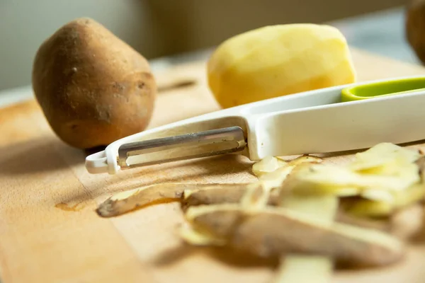 Peeler and potatoes with peelings on the table — Stock Fotó