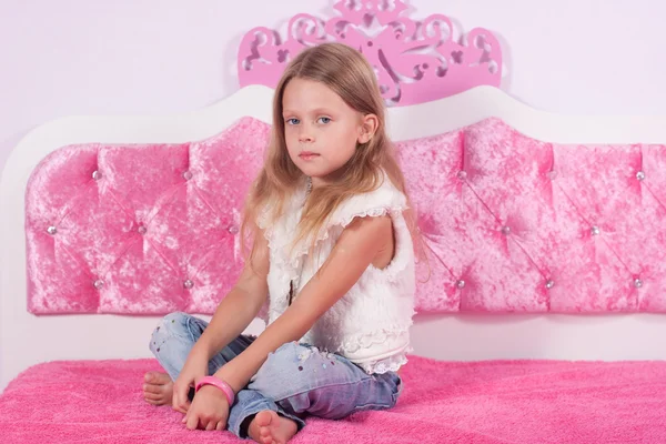 Little girl sitting on a pink bed — Stock Photo, Image