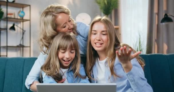 Momentos quentes de lazer familiar, onde atraente feliz sorrindo mãe despreocupada e suas duas idades diferentes filhas se divertindo juntos em casa durante o bate-papo de vídeo positivo no laptop — Vídeo de Stock