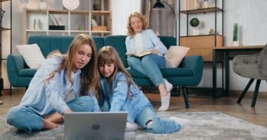 Güzel, sevgi dolu, mutlu, sarışın bir anne, en büyük ve en küçük kızlarıyla birlikte, bilgisayar oyunlarında kazandığı zaferi kaldırılmış elleriyle kutluyor.