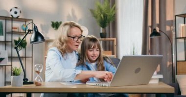 Çekici, yetenekli, sarışın annenin bilgisayardaki görevleri kullanarak pozitif kızına ödevlerinde yardım ettiği ev eğitimi kavramı.