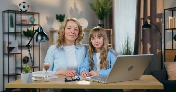 Familjeporträtt av härlig glad leende bekymmersfri blond mor och dotter som tittar in i kameran med nöjda ansiktsuttryck på heminredning bakgrund — Stockvideo