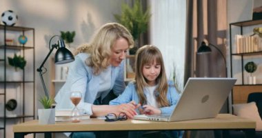 İyi görünümlü, iyi görünümlü, becerikli ve akıllı kızının ev ödevlerini yapmakla eğlenen iyi niyetli anneye yakın çekim.