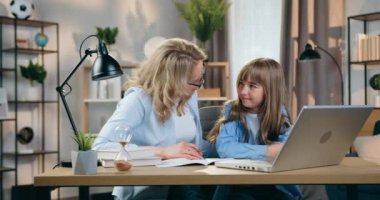 Güzel görünüşlü, güler yüzlü, mutlu, kaygısız, sarışın anne-kız iş yerinde bilgisayar başında oturuyor ve okul ödevlerini yapıyor.