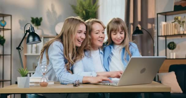 Concepto de ocio familiar donde adorable madre amorosa feliz y sus dos amables hijas de diferentes edades positivas sentadas frente a la computadora en la sala de estar contemporánea — Vídeos de Stock