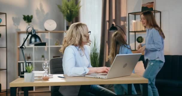 Attractive playful noisy two different ages sisters fooling around their serious busy skilled mother which working on laptop and making remarks them to be quieter,front view — Stock Video