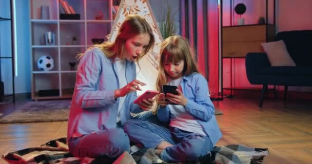 긍정적 이고 친근 한 나이의 여자 아이들은 침대 커버에 앉아 저녁에는 장식 용 비그님 방에 앉아서 스마트폰을 사용 합니다. — 비디오