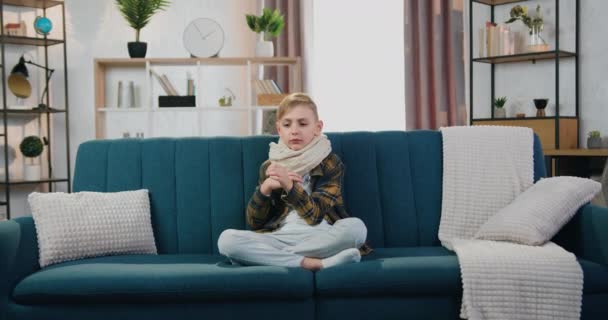Sağlık sigortası konsepti. Evdeki kanepede oturup vücut ısısını ölçen sevimli hasta çocuk termometrede yüksek göstergeler gördüğünde başını sallıyor. — Stok video