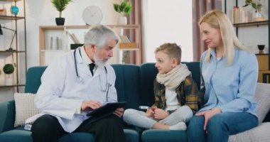 Çocuk sağlığı konsepti. Yakışıklı, arkadaş canlısı, yetenekli, sakallı bir doktorun hasta oğluyla konuşması ve ev ziyareti sırasında ona beşlik çakması.