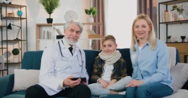 Çekici, olumlu, sakallı doktor ve sevgi dolu annesi olan hasta çocuk kameranın önünde oturmuş, çağdaş iç mimariye el sallıyor.