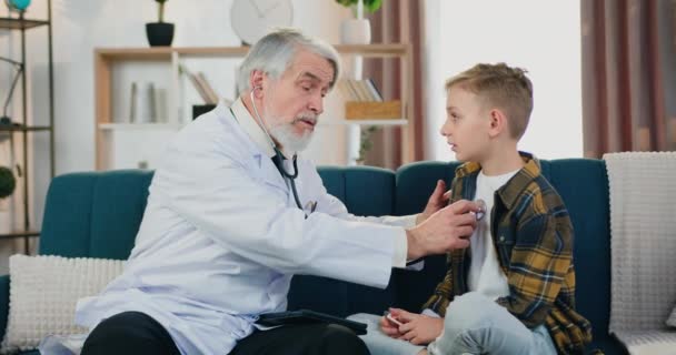 Aanzienlijke positieve tevreden gekwalificeerde volwassen bebaarde arts controleren hartslag van schattige tiener jongen patiënt tijdens een bezoek aan hem thuis, gezondheidszorg concept — Stockvideo
