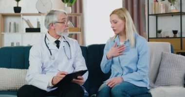 Hasta ruhlu bir kadının sağlık şikayetlerini dinlerken olgun sakallı aile doktorunun hasta kartına not aldığı doktorların ev ziyareti.